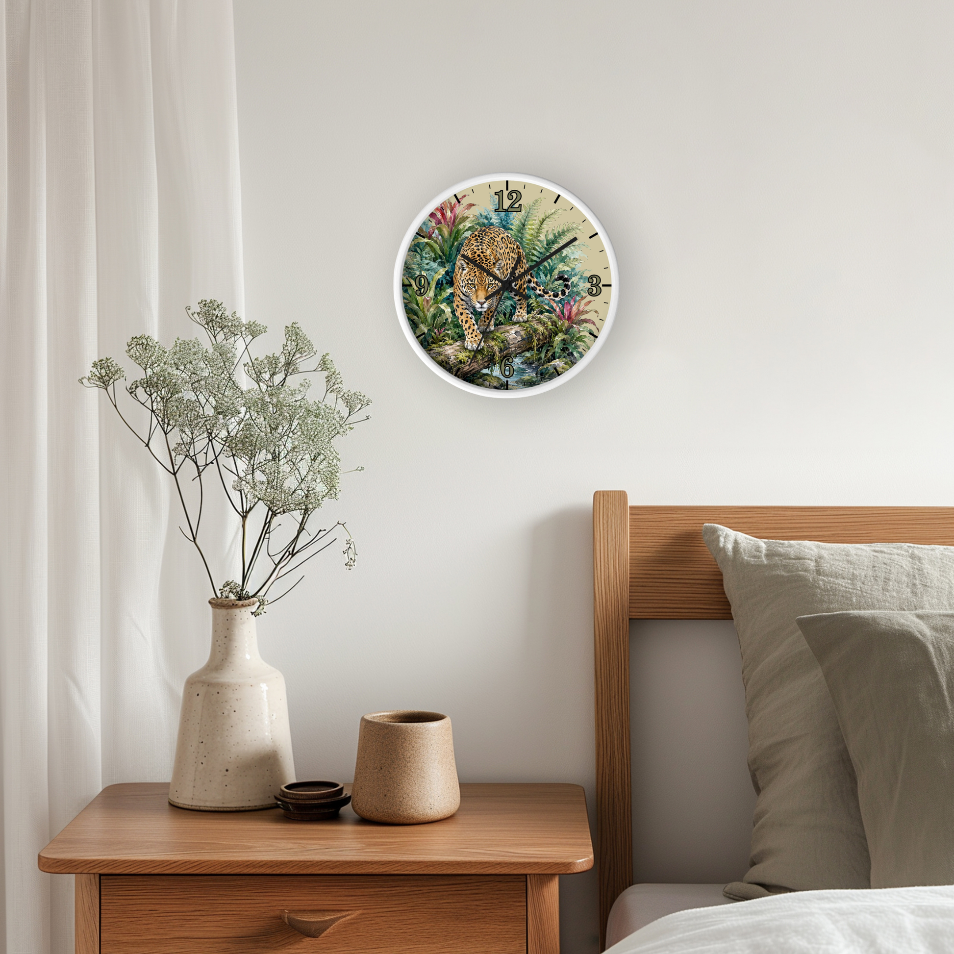 A round wall clock with a colorful jungle animal illustration hangs on a light gray bedroom wall above a wooden nightstand with a vase and candles, next to a bed with pillows.