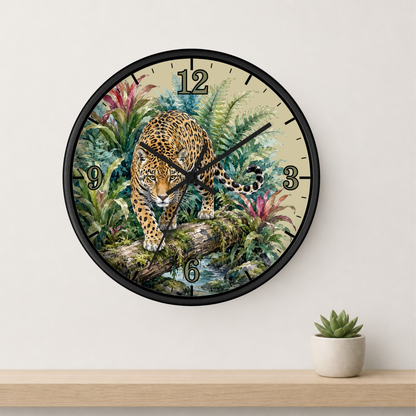 A round wall clock with a black frame and a detailed illustration of a leopard in a lush jungle scene. The clock is mounted on a white wall above a light wood shelf with a small potted succulent.