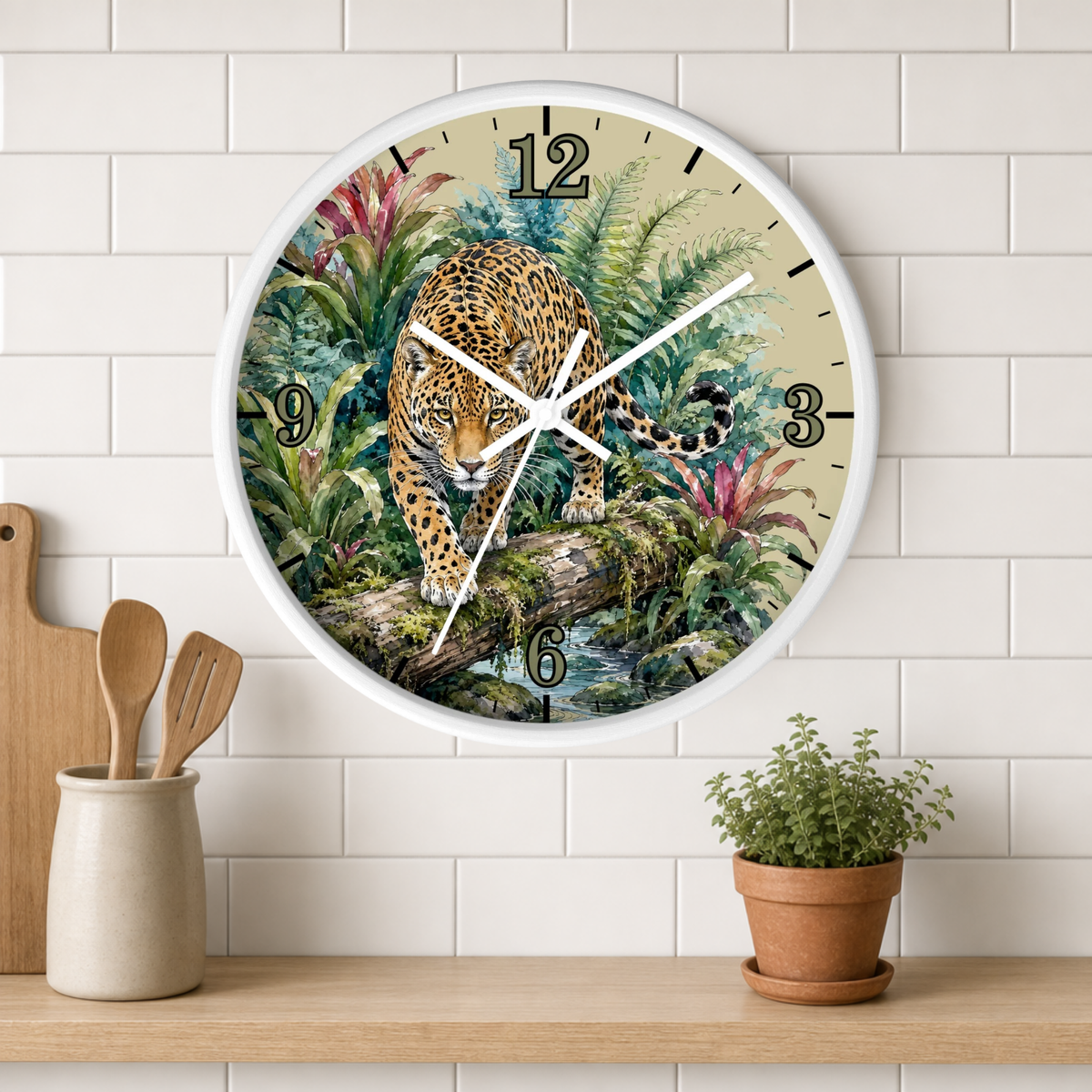 A round wall clock with a white frame and a detailed illustration of a leopard in a lush jungle, mounted on a white subway tile wall above a wooden shelf with a small potted plant and kitchen utensils.