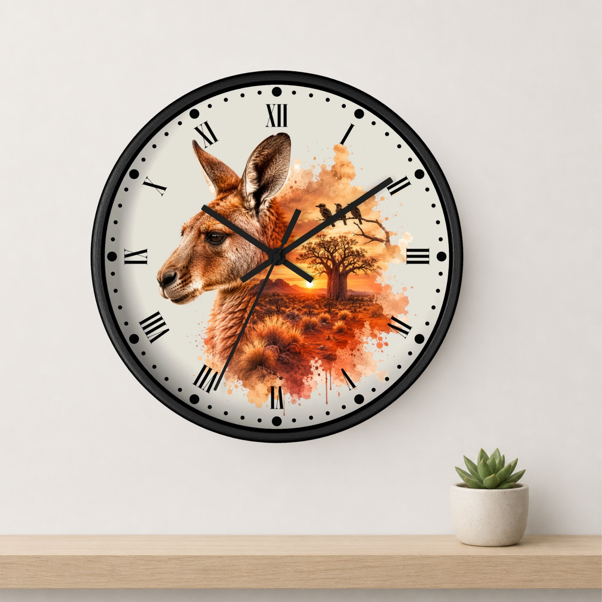 A round wall clock with a black frame and a white face featuring a kangaroo illustration over an orange autumn landscape. The clock is mounted on a light gray wall above a wooden shelf with a small potted succulent.