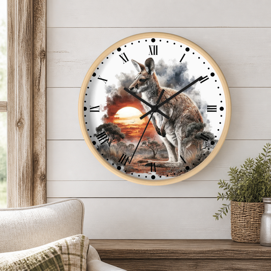 A round wall clock with a light wood frame hangs on a white shiplap wall above a wooden table. The clock face features a detailed illustration of a kangaroo standing in a sunset landscape with smoke and clouds.