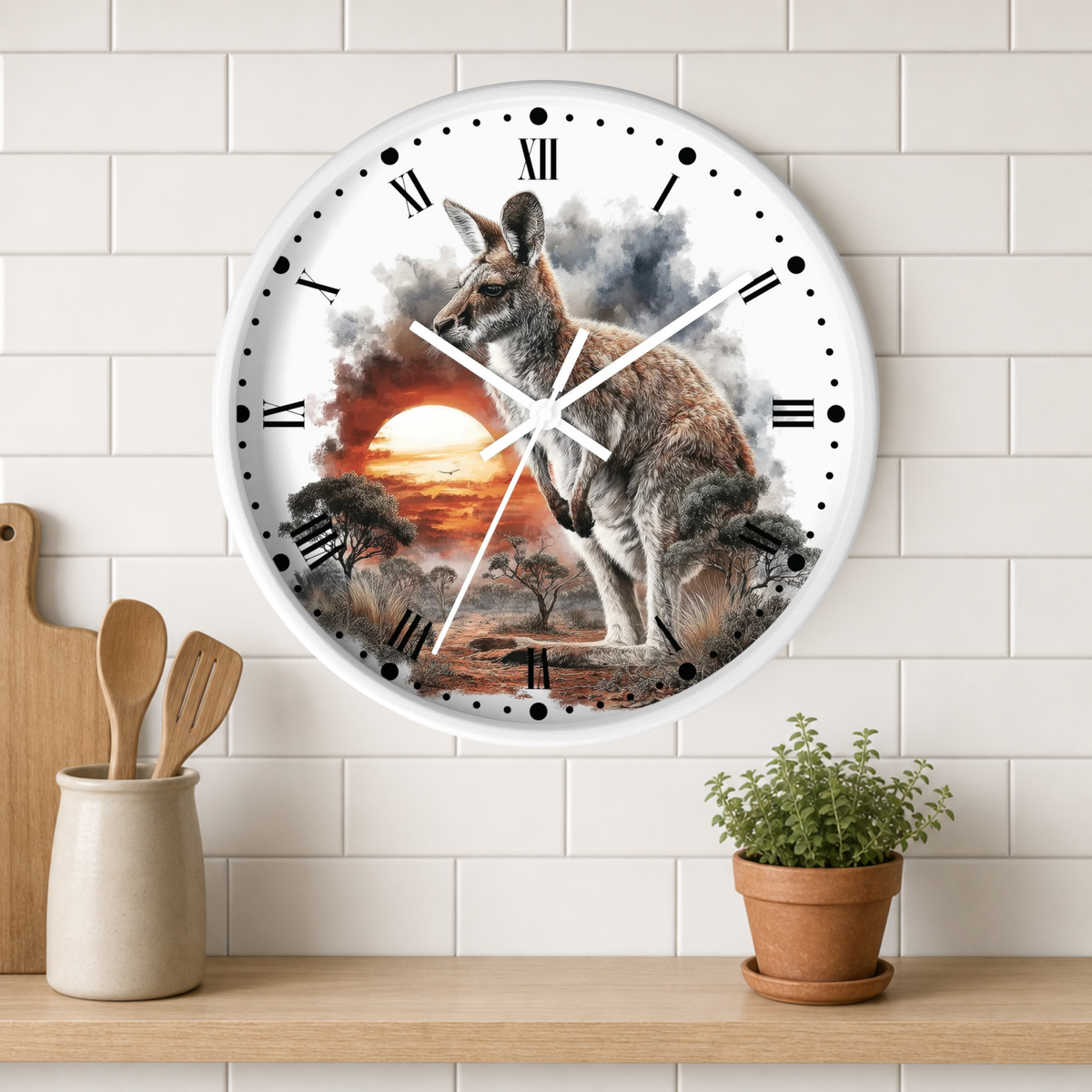 A round wall clock with a kangaroo and sunset landscape print, mounted on a white subway tile wall above a wooden shelf with kitchen utensils and a potted plant.