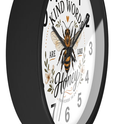 A close-up of a round wall clock with a black frame and a white face featuring a honeybee illustration, floral details, and the quote 'Kind words are like honey' with 'Honey' in script.