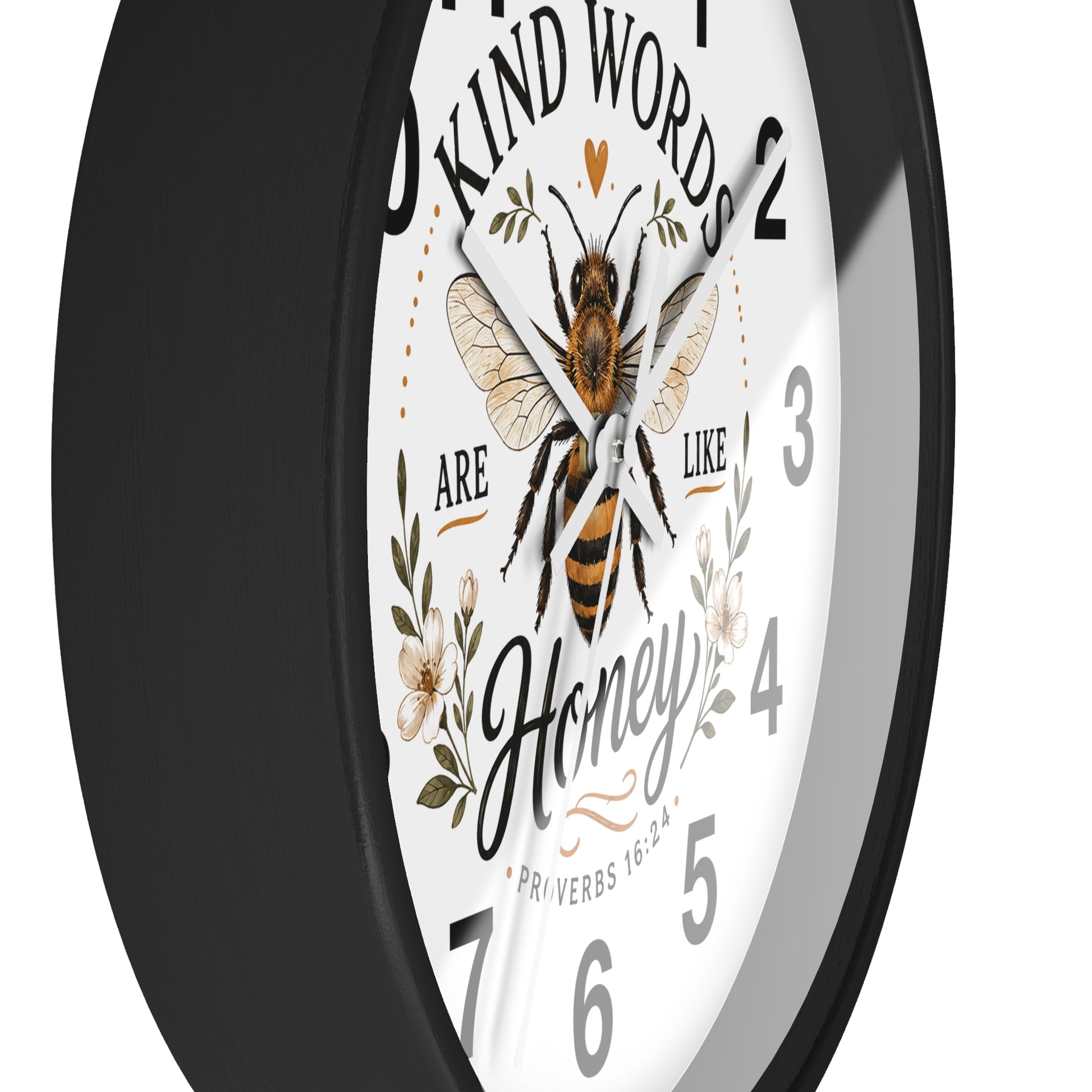 A round wall clock with a black frame and a white face featuring a bee illustration, floral details, and the quote 'Kind words are like honey' with scripture text.