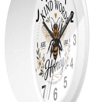 A white round wall clock with a printed bee and floral design on the face, featuring the quote 'Kind Words Are Like Honey' and black Arabic numerals.