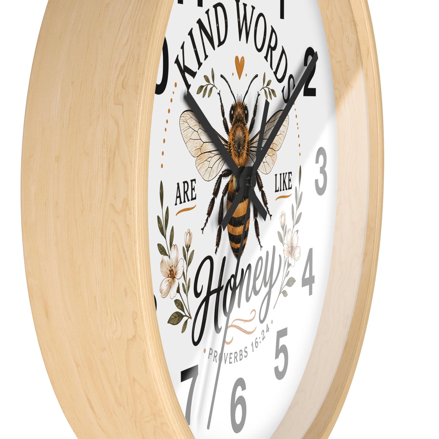 A round wall clock with a light natural wood frame, a white face, and a central illustration of a honeybee surrounded by floral elements and the words 'Kind Words Are Like Honey'.