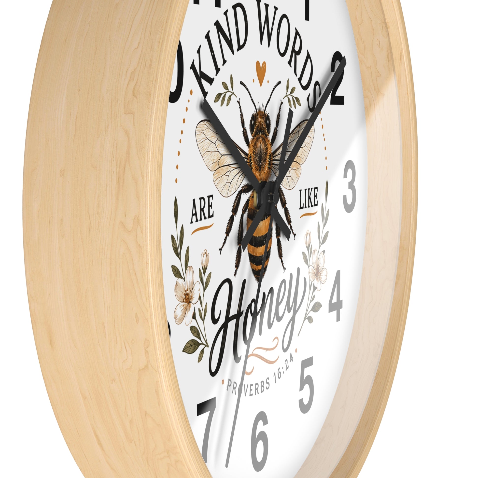 A round wall clock with a light natural wood frame, a white face, and a central illustration of a honeybee surrounded by floral elements and the words 'Kind Words Are Like Honey'.