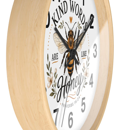 A round wall clock with a light natural wood frame, a white face, and a central illustration of a honeybee surrounded by floral elements and the words 'Kind Words Are Like Honey'.