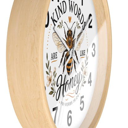 A close-up of a round wall clock with a light natural wood frame and a white face. The clock face features a detailed illustration of a honeybee, floral elements, and the text 'KIND WORDS ARE LIKE Honey' with numbers in black.