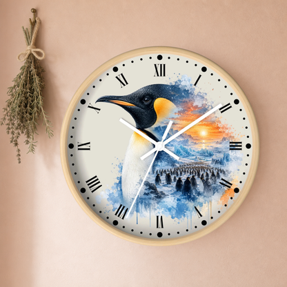 A round wall clock with a light wood frame and Roman numerals, featuring a colorful penguin illustration over a blue and orange watercolor landscape. The clock is mounted on a beige wall next to a small hanging bunch of dried herbs.