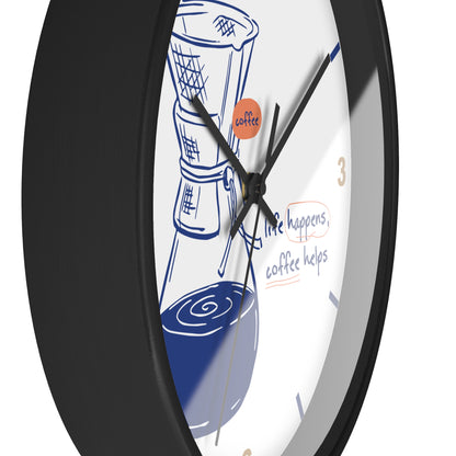 A close-up of a round wall clock with a black frame and a white face featuring a blue coffee maker illustration, handwritten-style text reading 'life happens, coffee helps,' and a small orange circle with the word 'coffee.'.