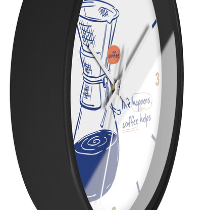 A close-up of a round wall clock with a black frame and a white face featuring a coffee maker illustration, blue coffee cup graphics, and the phrase 'life happens, coffee helps'.