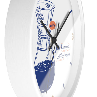 A white round wall clock with a coffee-themed illustration and text on the face. The design features a blue coffee cup and bean bag, a small orange circle with the word 'coffee', and the phrase 'life happens, coffee helps' in blue and orange script.