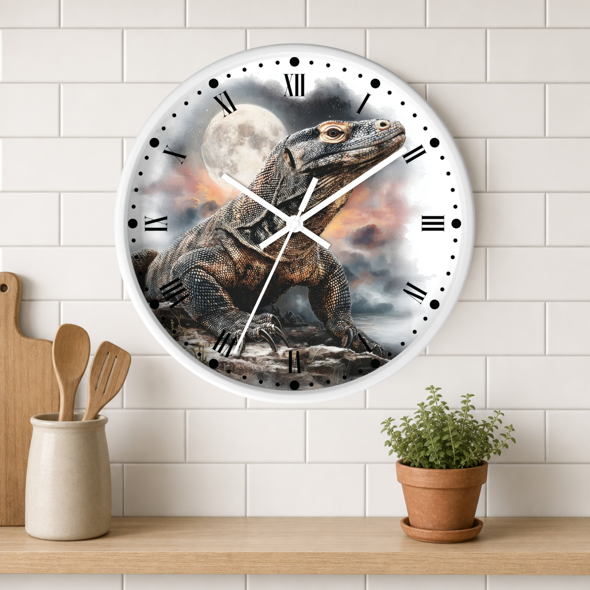 A round wall clock with a white frame and Roman numerals, featuring a detailed illustration of a large lizard under a full moon on the face. The clock is mounted on a white subway-tile wall above a wooden shelf with a small potted plant and wooden utensils.