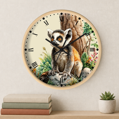 A round wall clock with a light wood frame and a detailed illustration of a ring-tailed lemur sitting in front of a tree trunk, displayed on a beige wall above a shelf with books and a small potted succulent.