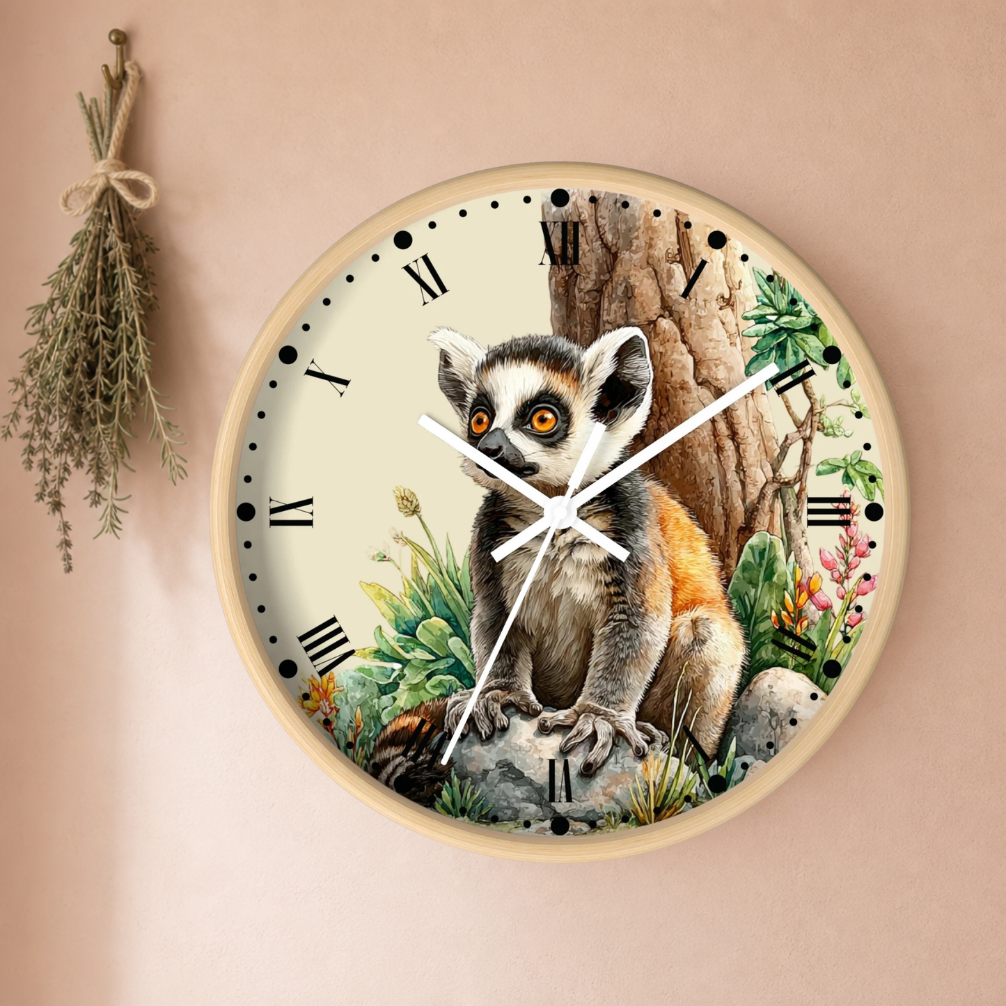 A round wall clock with a natural wood frame, featuring a detailed illustration of a ring-tailed lemur sitting in front of a tree trunk. The clock face has an off-white background with black Roman numerals and white clock hands, mounted on a warm beige wall next to a dried herb sprig.