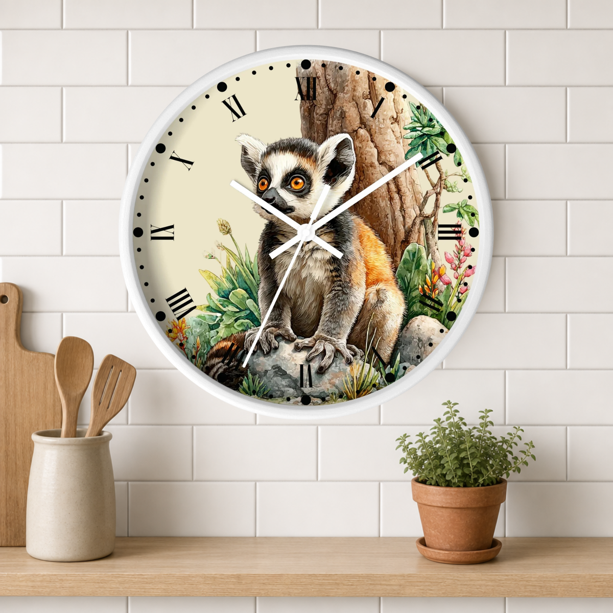 A round wall clock with a white frame and a detailed illustration of a lemur sitting in front of a tree, displayed on a white subway tile wall above a wooden shelf with a small potted plant and wooden utensils.