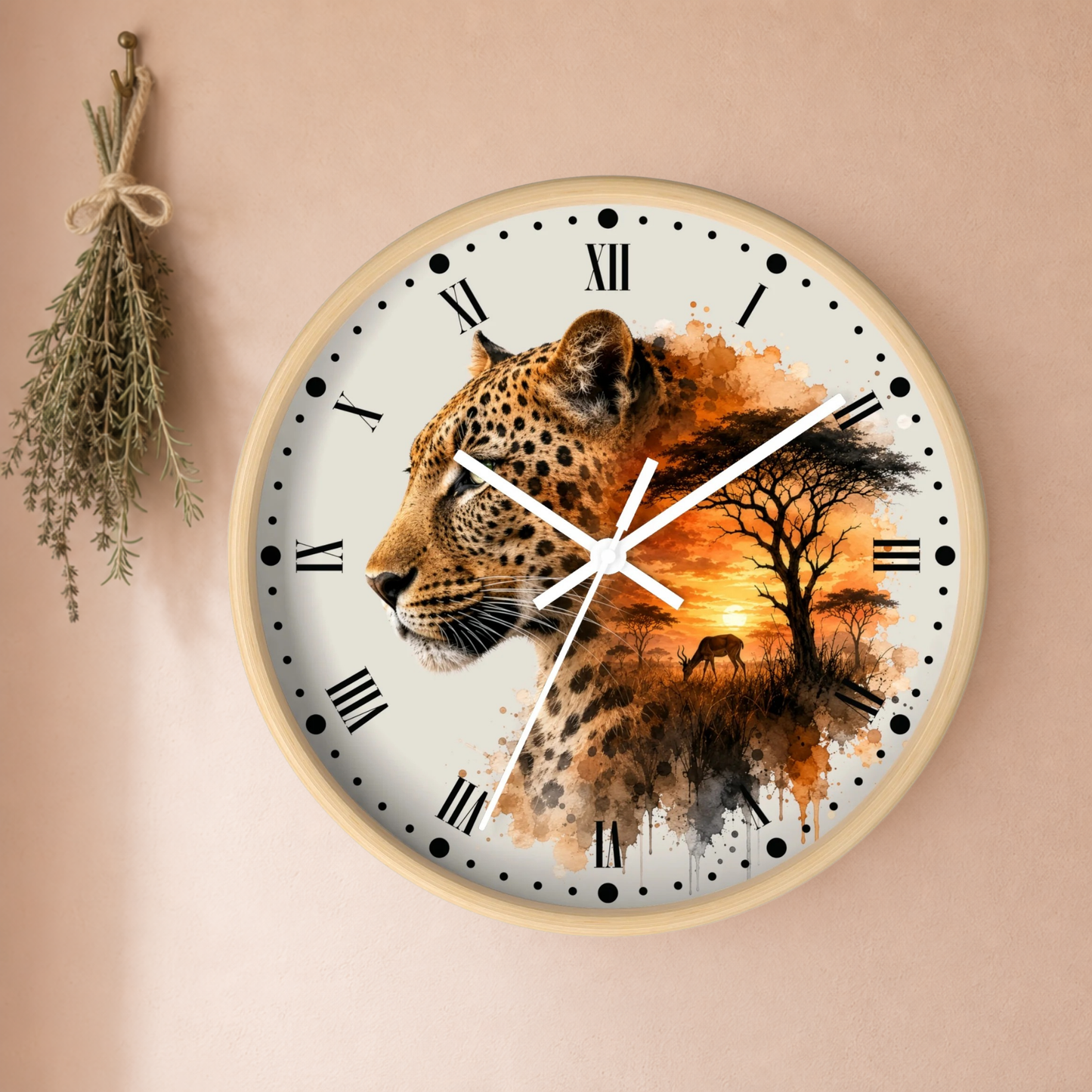 A round wall clock with a light wood frame, featuring a printed design of a leopard in profile blending into an African savanna sunset scene. The clock is mounted on a warm beige wall next to a hanging sprig of dried herbs.