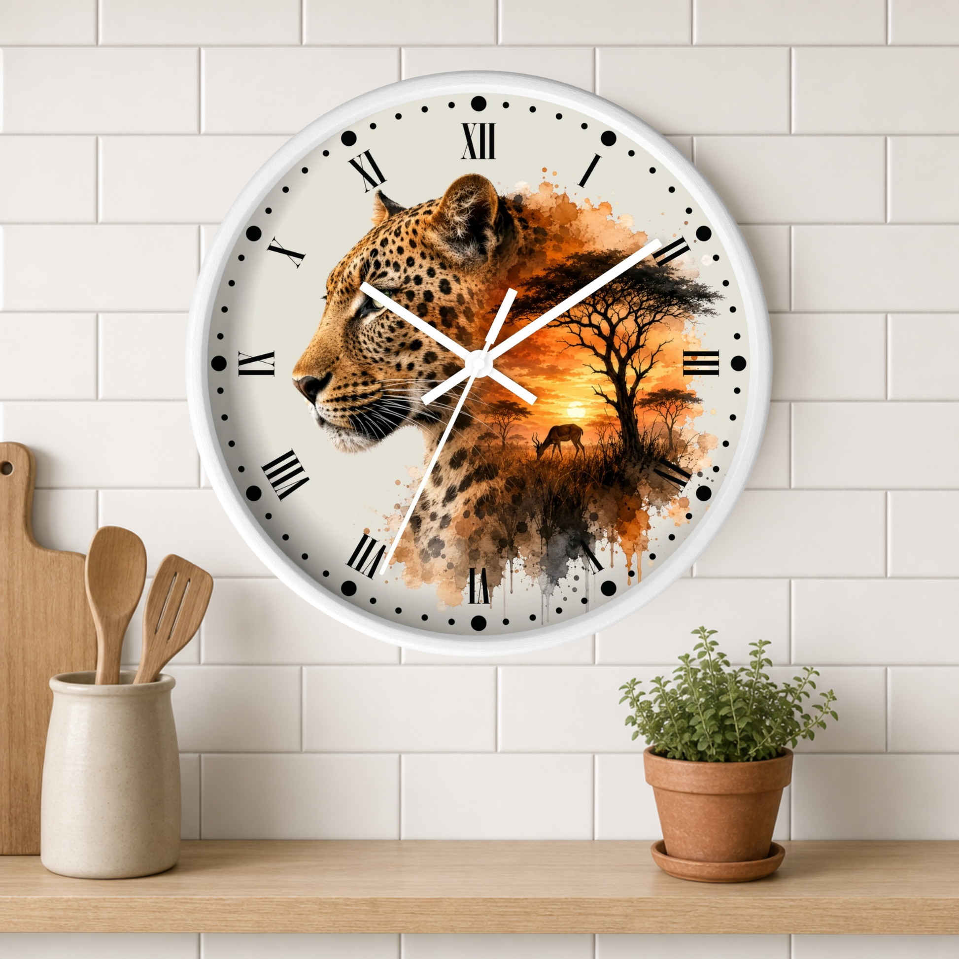 A round wall clock with a white frame and Roman numerals, featuring a printed design of a leopard's face blended with an orange sunset landscape and tree silhouette. The clock is mounted on a white subway-tile wall above a wooden shelf with a small potted plant and wooden utensils.