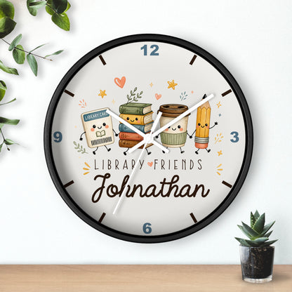 A personalized round wall clock with a black frame and a whimsical library-themed face. The clock features cute cartoon illustrations of books, a coffee cup, a pencil, and a small library card character, with the text 'LIBRARY FRIENDS' and the name 'Johnathan' in cursive.