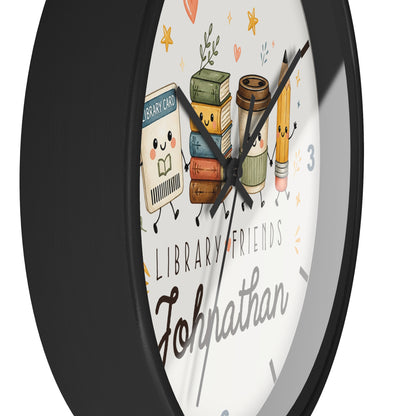 A round wall clock with a black frame and a white face featuring cute illustrated library-themed characters, including books, a coffee cup, and a pencil, with the text 'LIBRARY FRIENDS' and the name 'Johnathan'.