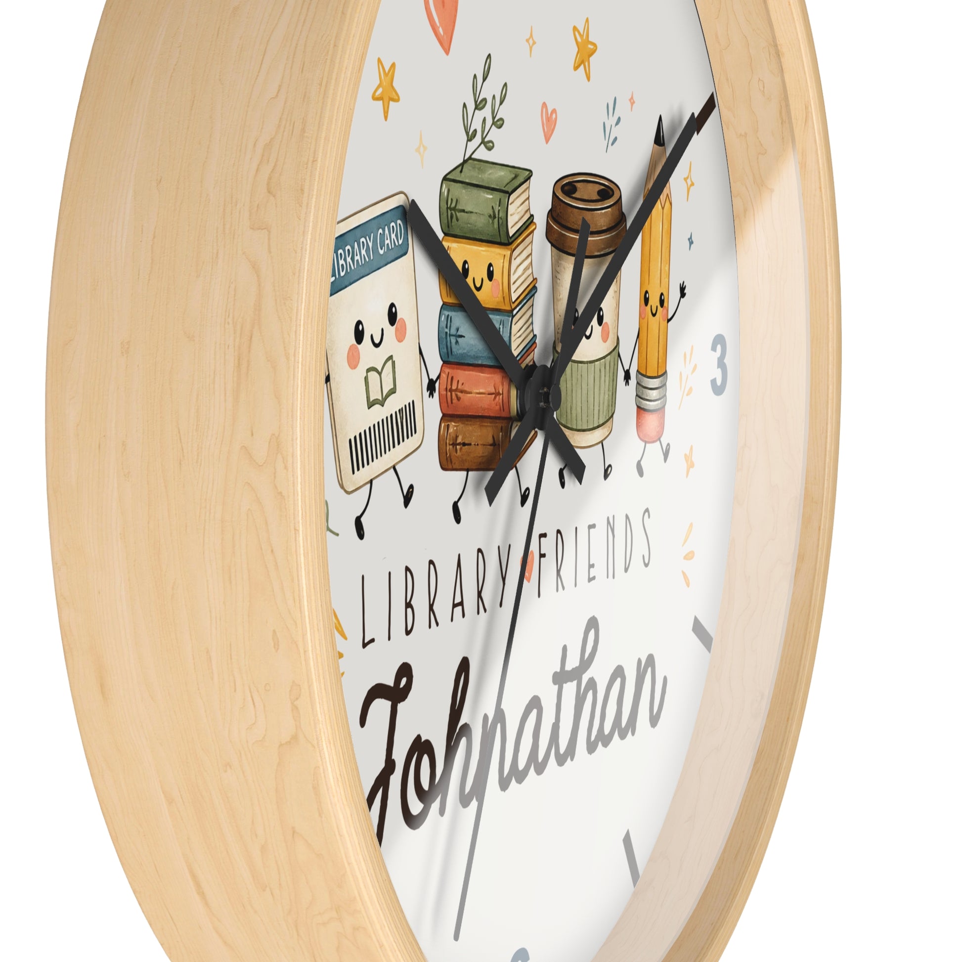 A round wall clock with a light natural wood frame and a white face featuring cute illustrated library-themed characters, including books, a pencil, and a card, with the text 'LIBRARY FRIENDS' and 'Johnathan'.