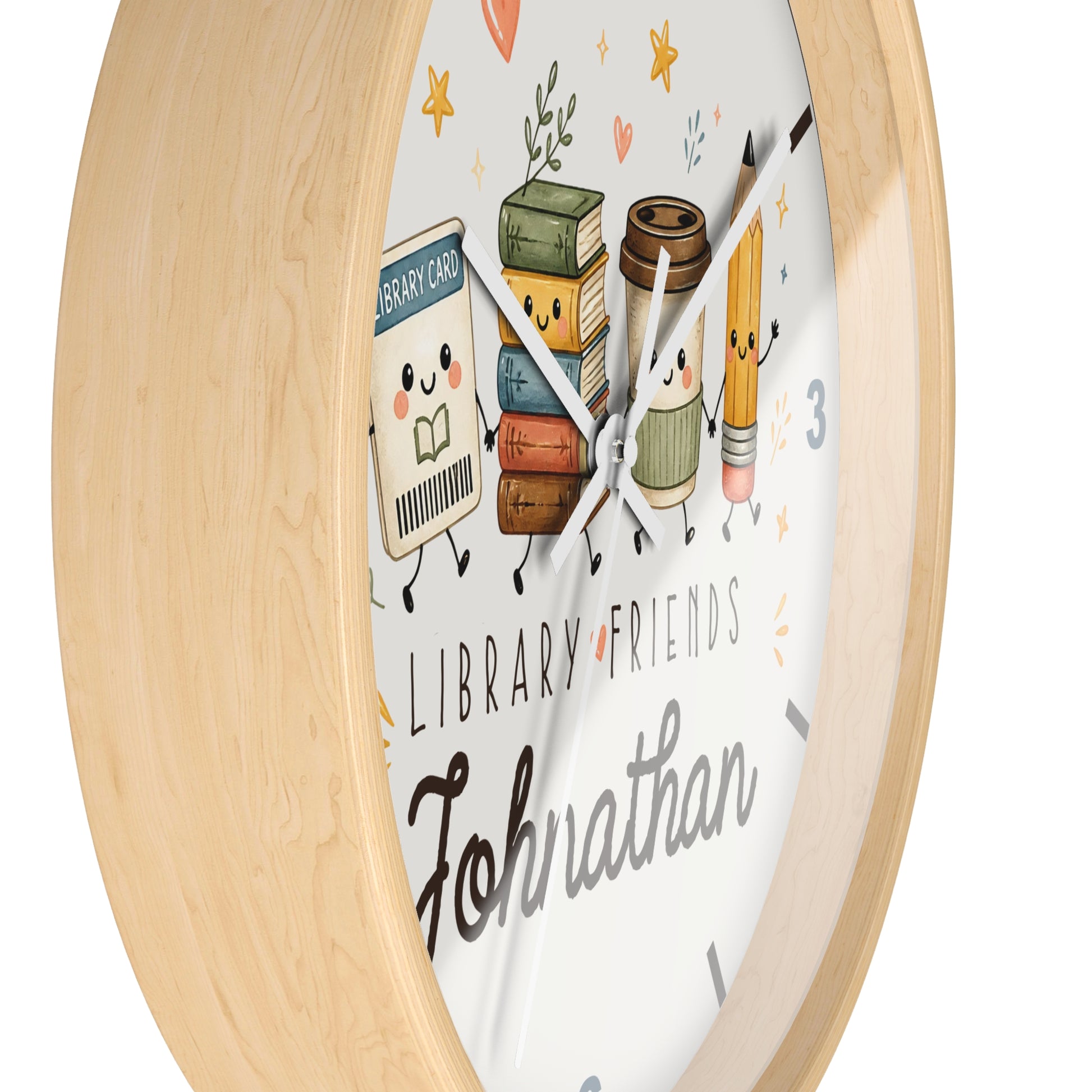 A round wall clock with a light natural wood frame and a white face featuring cute cartoon library-themed illustrations, including books, a coffee cup, a pencil, and the text 'LIBRARY FRIENDS' and 'Johnathan'.