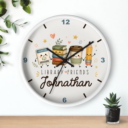 A personalized round wall clock with a white frame, featuring a cute library-themed illustration with books, a coffee cup, and a pencil. The clock face has the text 'LIBRARY FRIENDS' and the name 'Johnathan' in script.