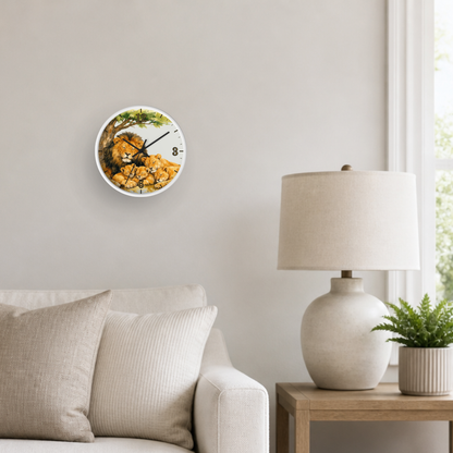 A round wall clock with a printed watercolor lion family design hangs on a light gray wall above a beige sofa. A white table lamp and a small potted plant sit on a wooden side table next to a window.