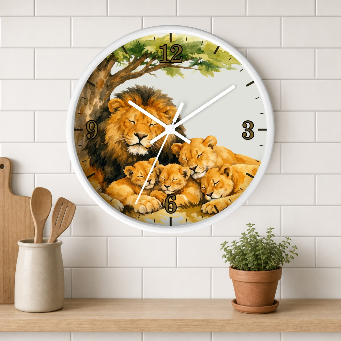 A round wall clock with a white frame and a printed illustration of lions under a tree, mounted on a white subway-tile wall above a wooden shelf with a small potted plant and utensils.