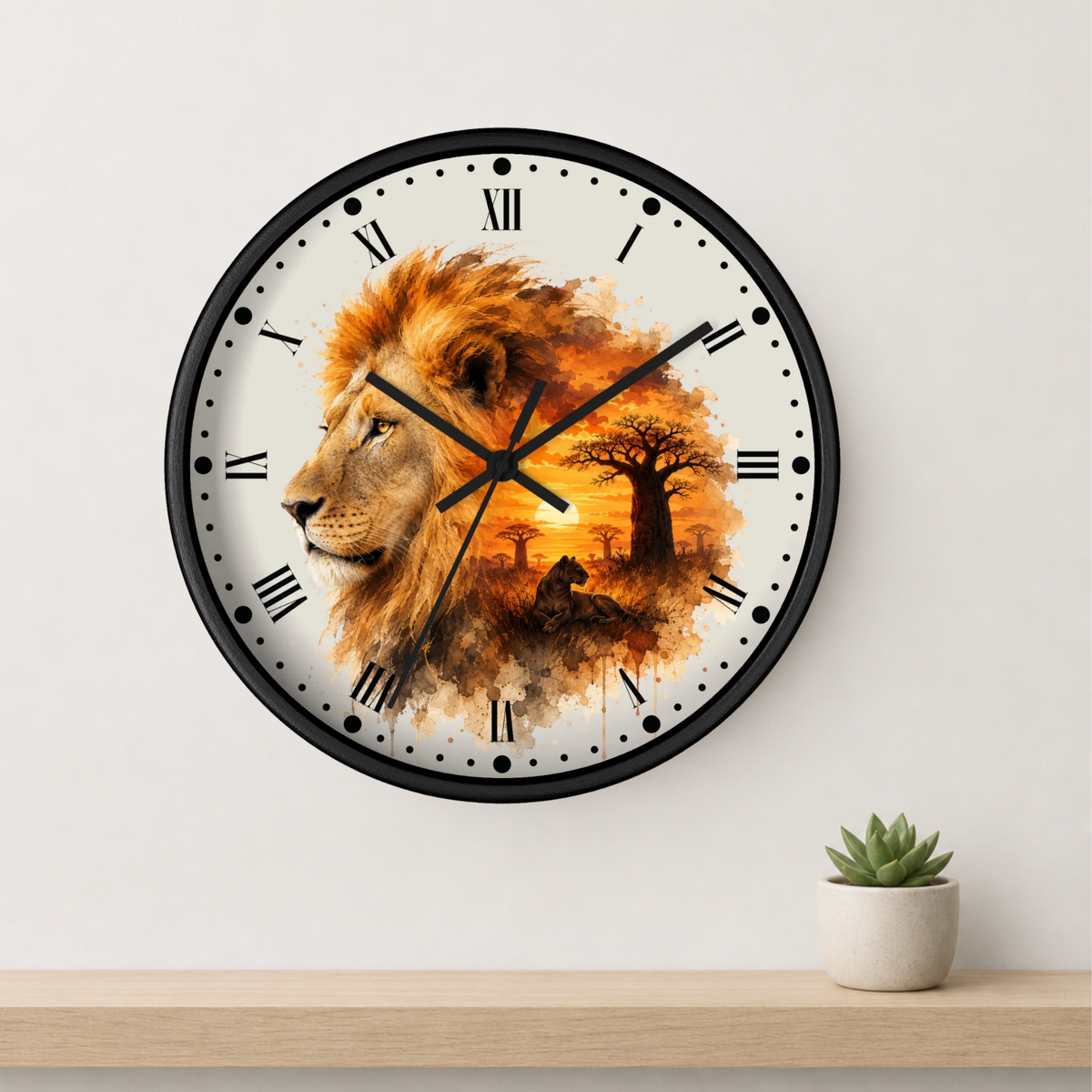 A round wall clock with a black frame and a white face featuring a watercolor-style lion portrait in warm orange, brown, and gold tones. The clock is mounted on a light wall above a wooden shelf with a small potted succulent.