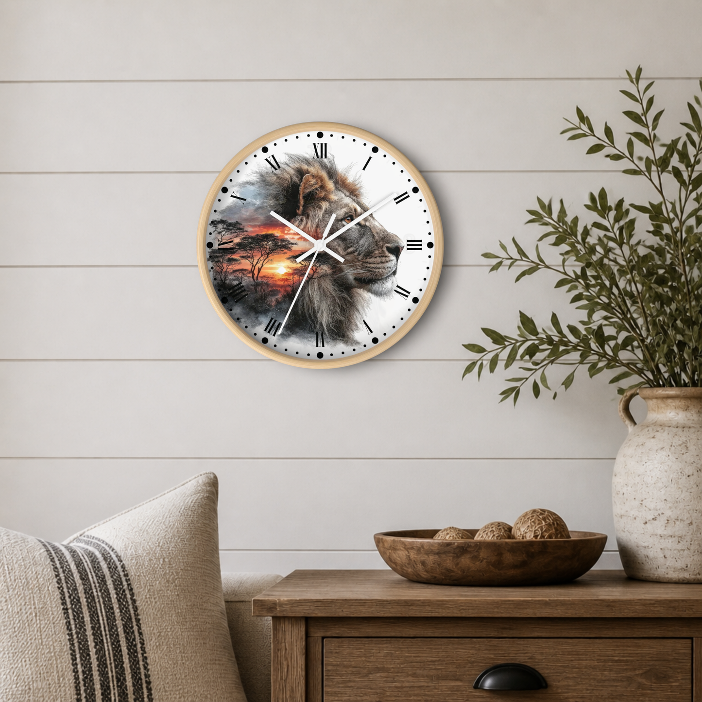 A round wall clock with a light wood frame hangs on a white shiplap wall above a wooden side table. The clock face features a detailed lion illustration with a sunset scene.