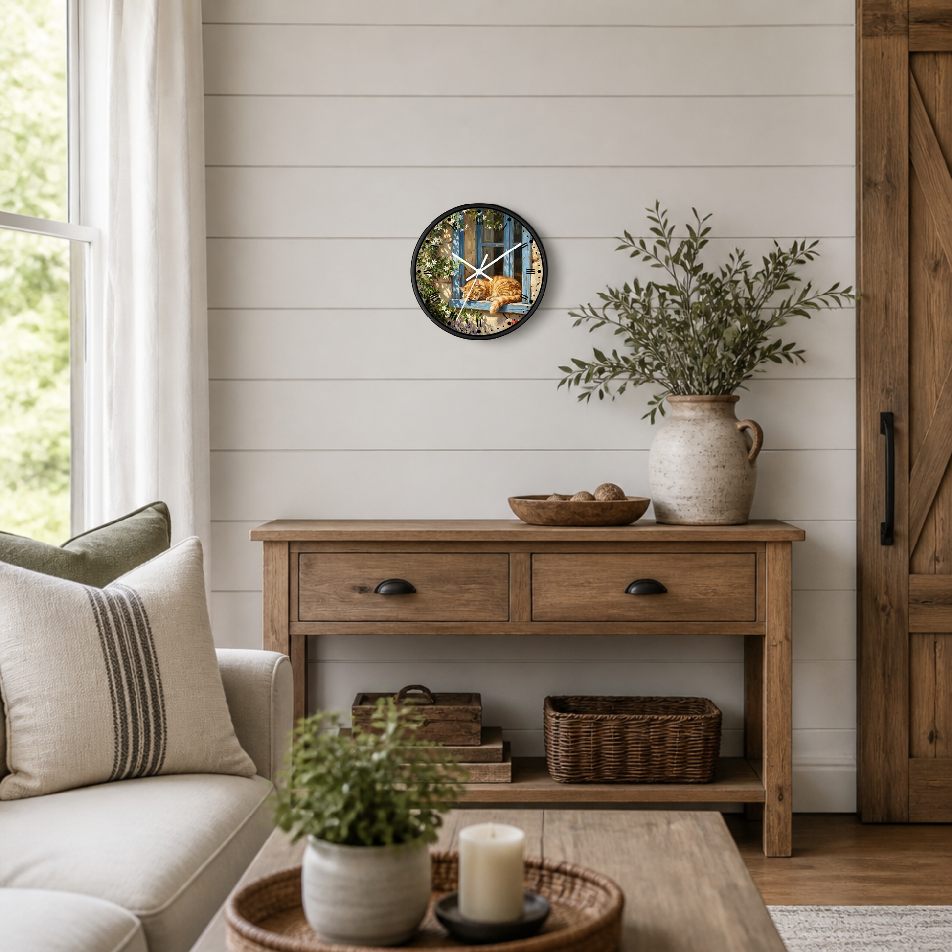 A round wall clock with a colorful orange cat sleeping in a window print and white clock hands, hanging on a white shiplap wall above a rustic wooden console table in a bright, modern farmhouse living room.