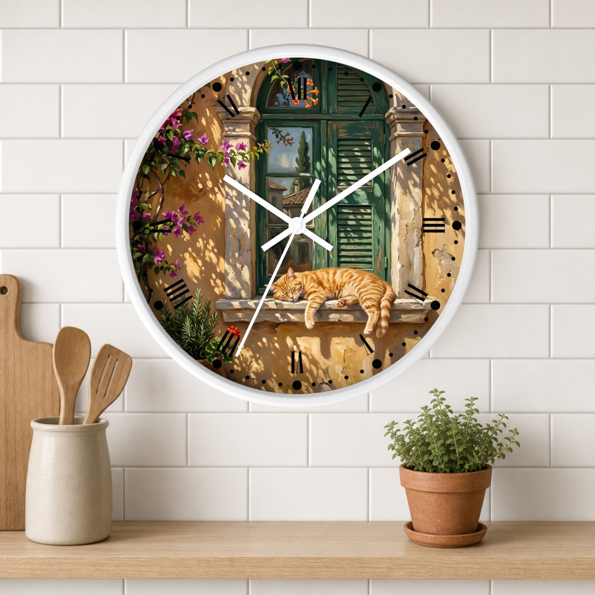 A round wall clock with a white frame hangs on a white subway-tile wall above a wooden shelf. The clock face features a detailed illustration of a warm courtyard scene with a sleeping orange tabby cat on a windowsill, green shutters, flowers, and shadow play.