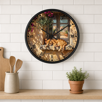 A round wall clock with a black frame and a printed scene of an orange tabby cat sleeping by a window, mounted on a white subway tile wall above a wooden shelf with kitchen utensils and a potted plant.
