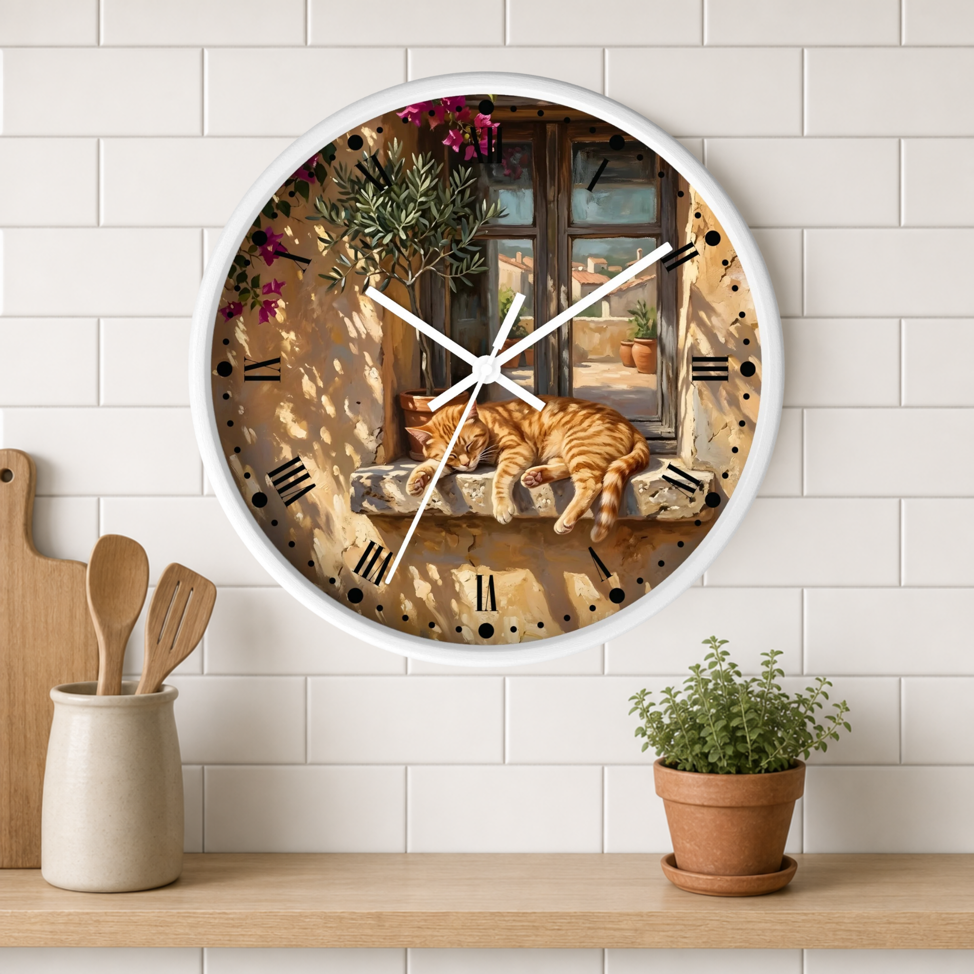 Round wall clock with a white frame and a printed scene of an orange tabby cat sleeping on a stone windowsill, mounted on a white subway tile wall above a wooden shelf with kitchen utensils and a potted plant.