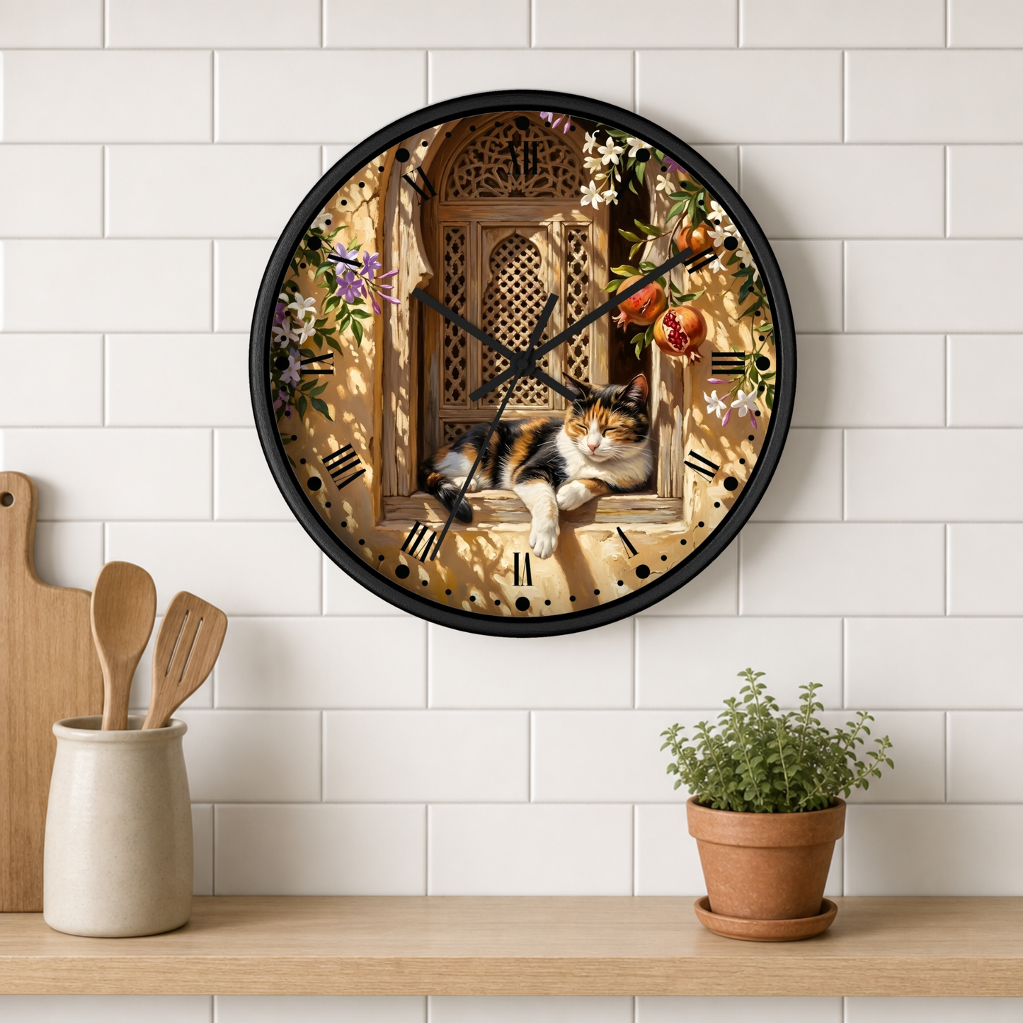 A round wall clock with a black frame and a printed design of a cat lounging in an ornate window surrounded by flowers and fruit, mounted on a white subway tile wall above a wooden shelf with kitchen utensils and a potted plant.