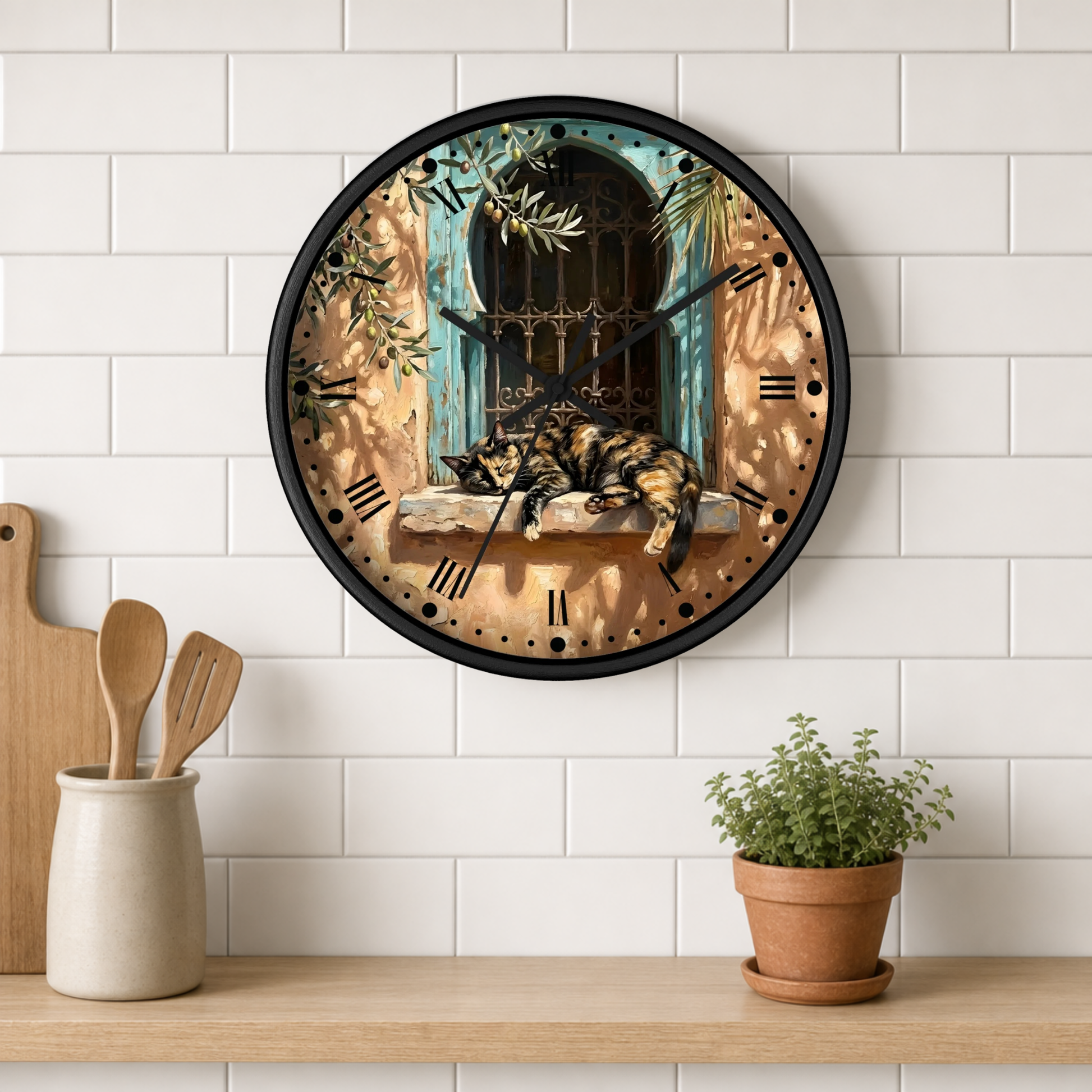 A round wall clock with a black frame hangs on a white subway tile wall above a wooden shelf. The clock face features a scenic illustration of a cat sleeping on a windowsill with a turquoise window and warm brown tones.