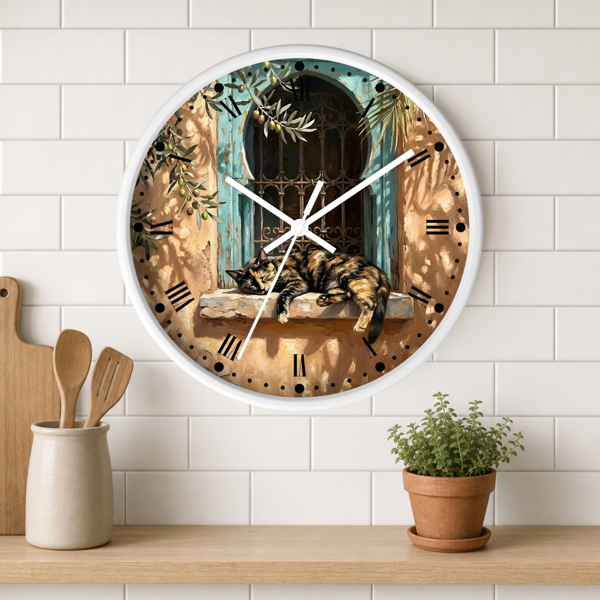 A round wall clock with a white frame hangs on a white subway tile wall above a wooden shelf. The clock face features an illustration of a sleeping cat on a windowsill with a turquoise window and olive branches.