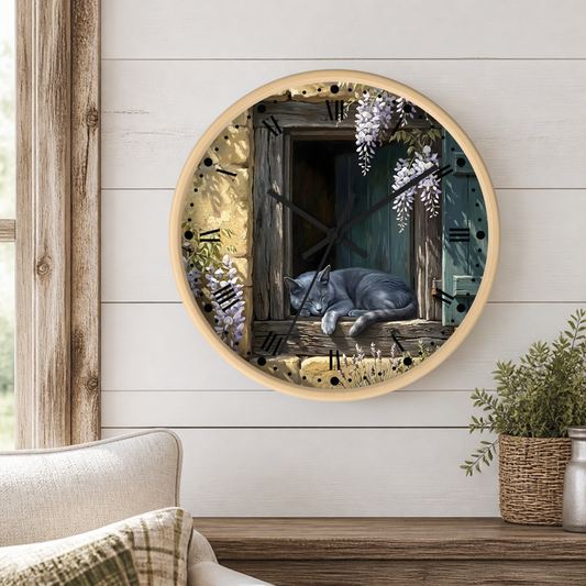 Round wall clock with a light wood frame, featuring a printed illustration of a gray cat sleeping by an open rustic window with wisteria flowers, mounted on a white shiplap wall above a wooden mantel with a plant.
