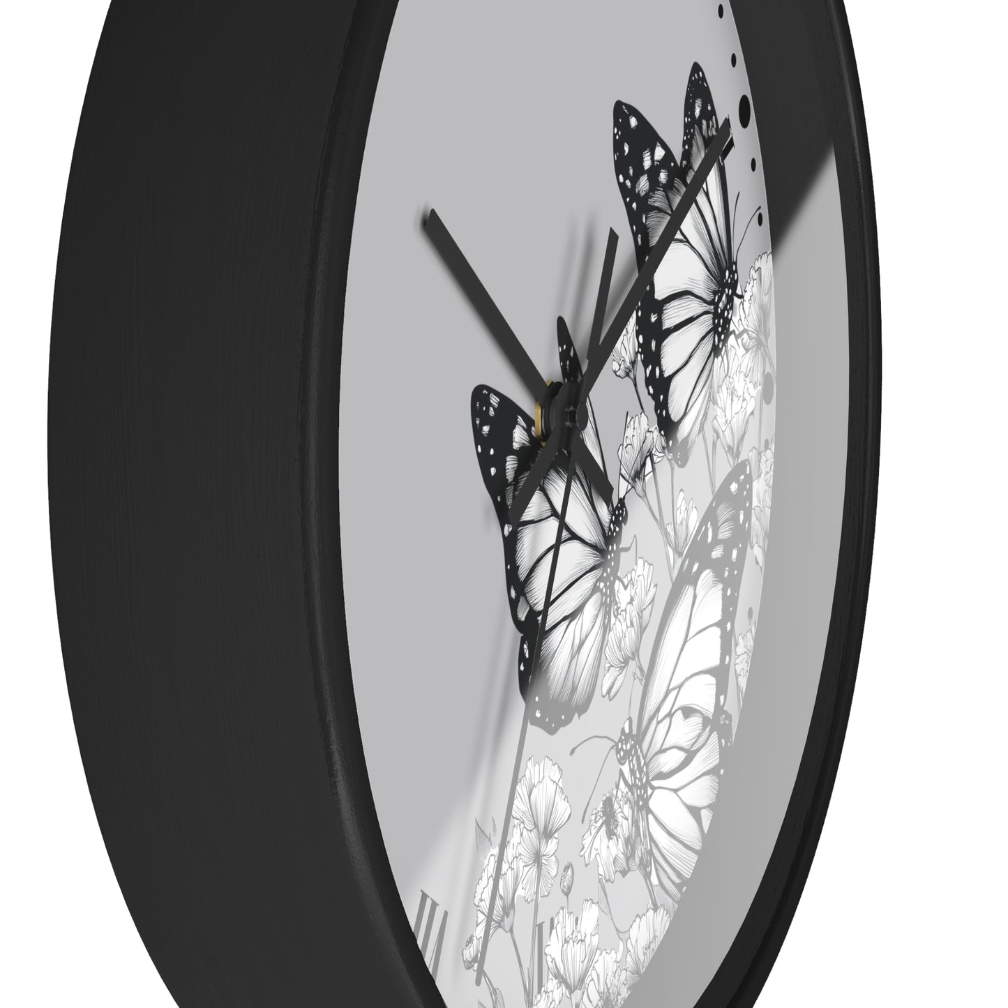 A close-up of a round wall clock with a matte black frame and a white dial decorated with black-and-white butterfly and floral illustrations.