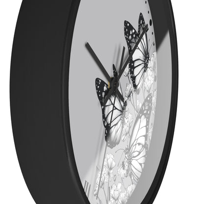 A close-up of a round wall clock with a matte black frame and a white dial decorated with black-and-white butterfly and floral illustrations.
