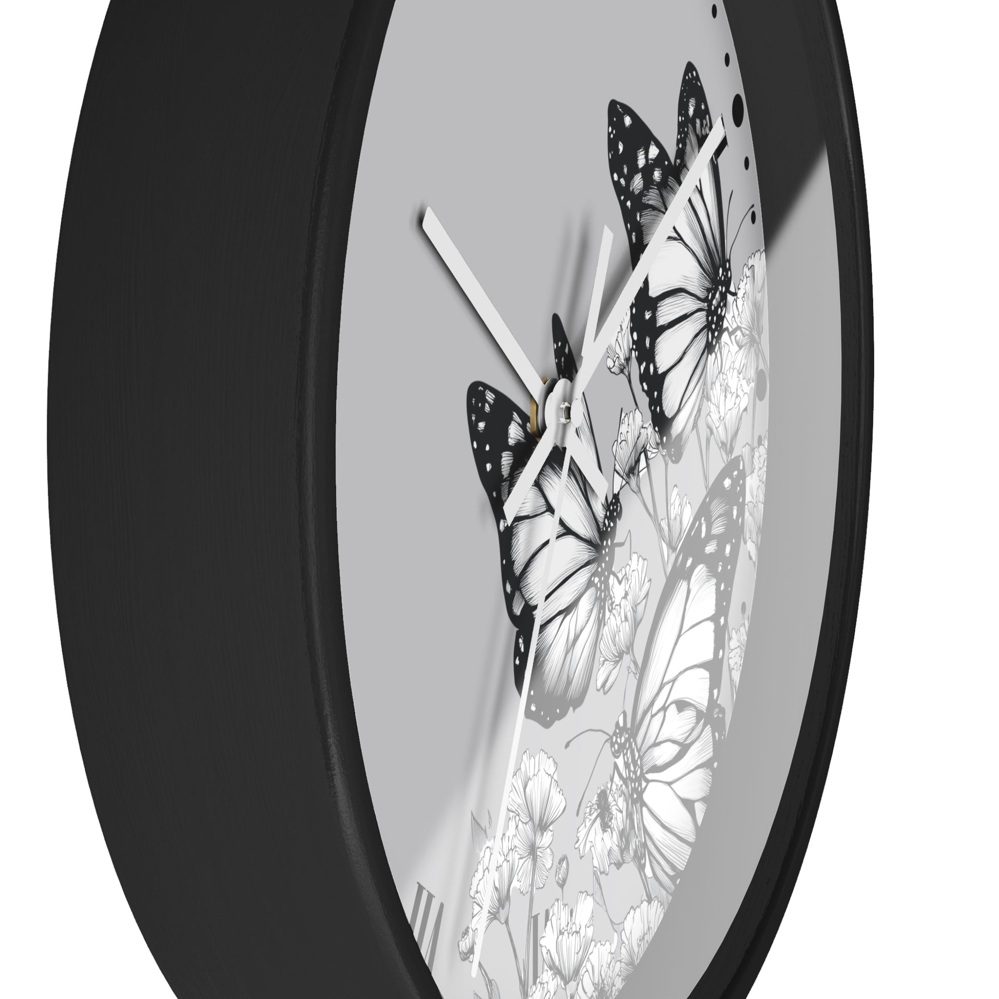 A close-up of a round wall clock with a matte black frame and a light gray face featuring black-and-white butterfly and floral illustrations.