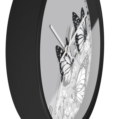 A close-up of a round wall clock with a matte black frame and a light gray face featuring black-and-white butterfly and floral illustrations.