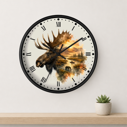 A round wall clock with a black frame and a white face featuring a moose head and autumn landscape illustration, mounted on a light wall above a wooden shelf with a small potted succulent.