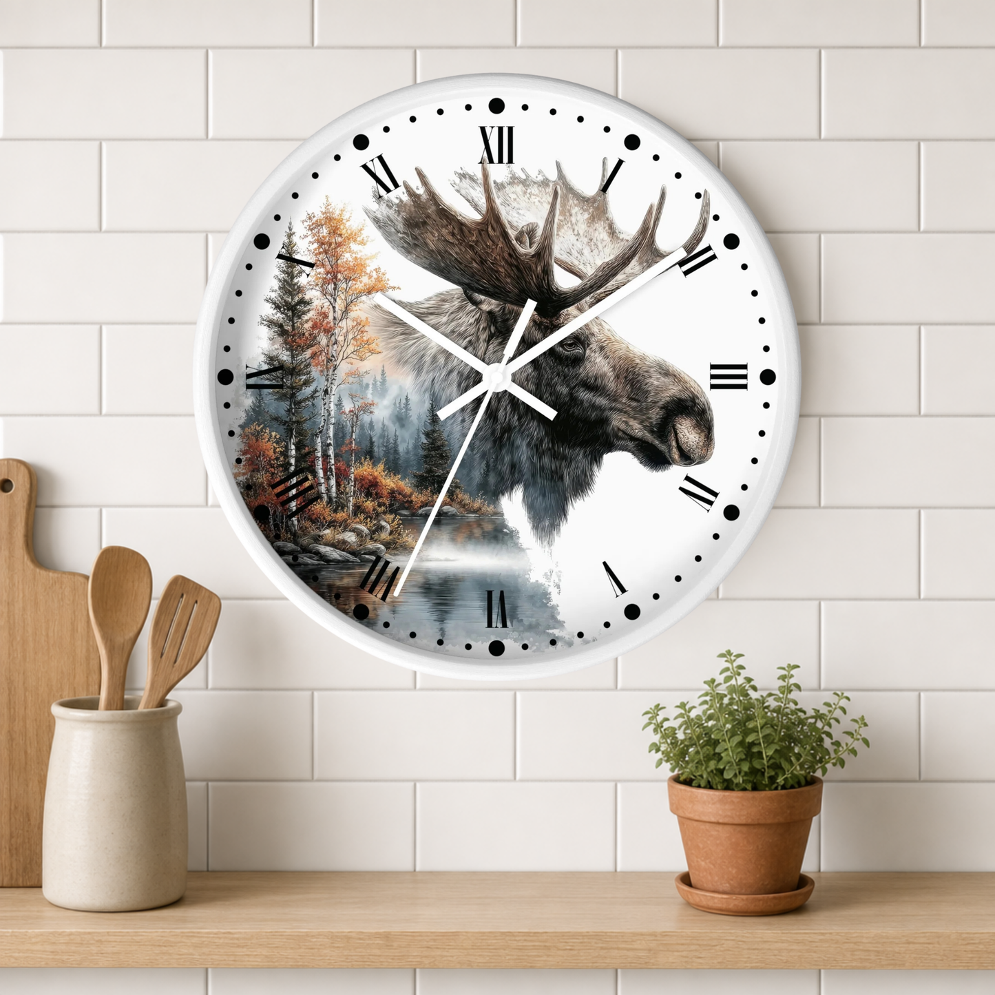 A round wall clock with a moose head and forest landscape printed on the face, mounted on a white subway-tile wall above a wooden shelf with a small potted plant and kitchen utensils.