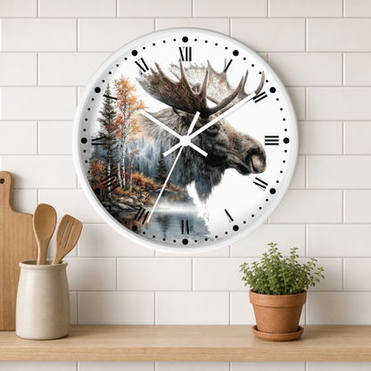 A round wall clock with a moose head and forest landscape printed on the face, mounted on a white subway-tile wall above a wooden shelf with a small potted plant and kitchen utensils.