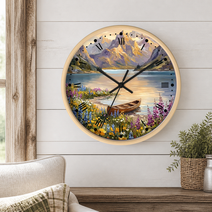 A round wall clock with a light wood frame hangs on a white shiplap wall above a wooden table. The clock face features a scenic landscape illustration with mountains, a lake, wildflowers, and a small rowboat.