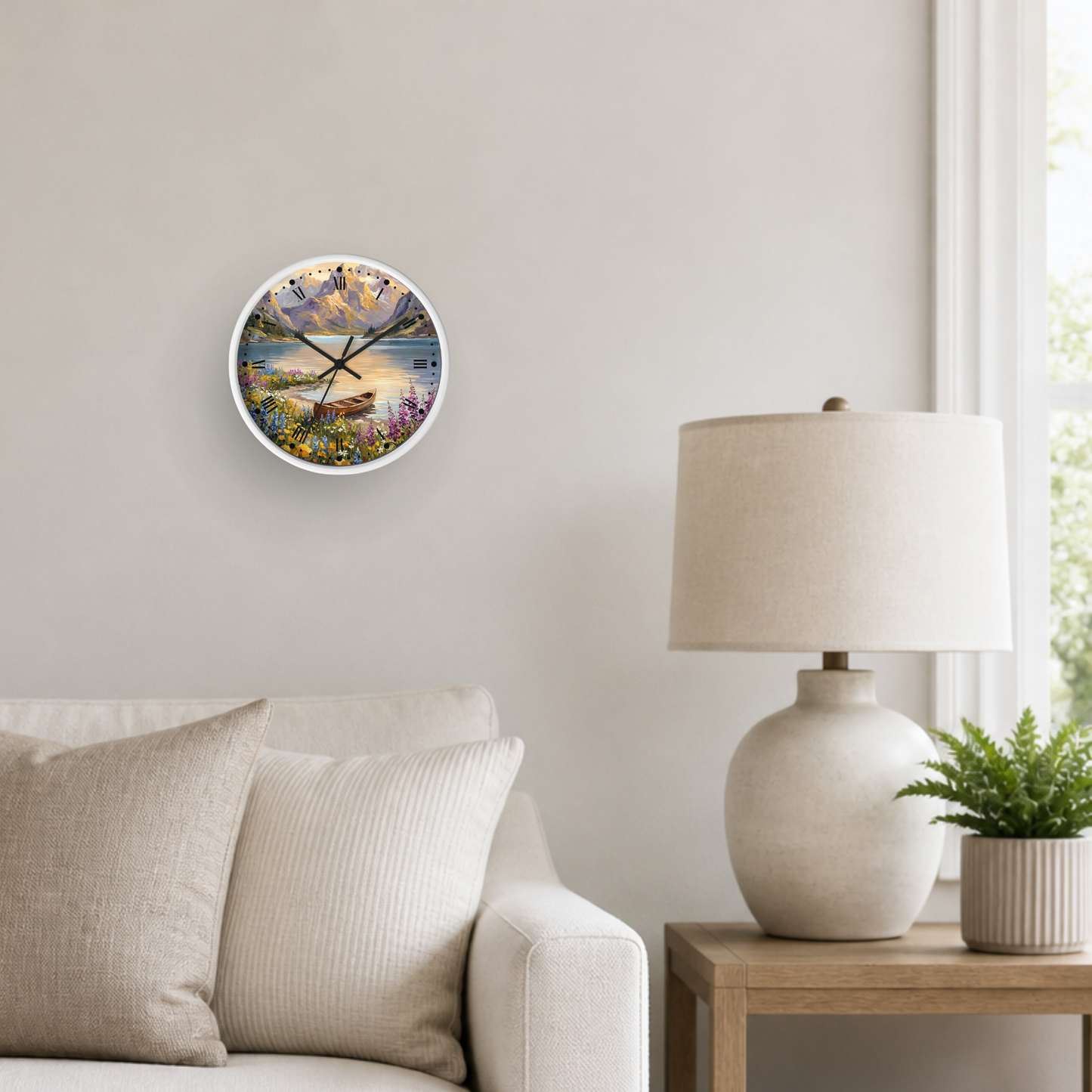 A round wall clock with a colorful landscape print hangs on a light beige wall in a styled living room setting next to a white table lamp and a small potted plant.