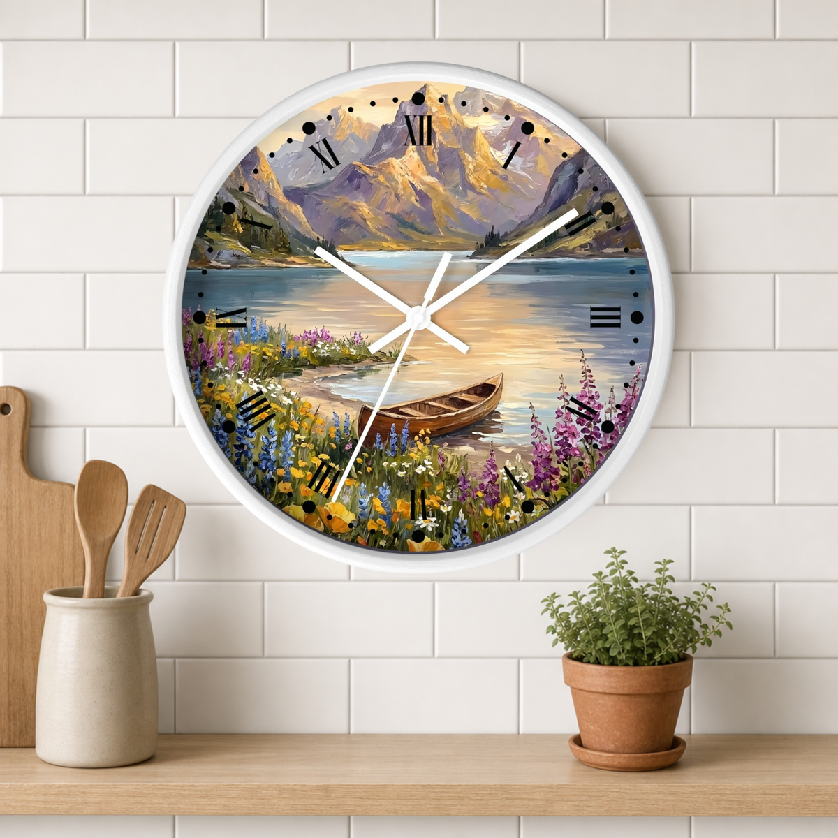 A round wall clock with a white frame and a scenic landscape print featuring mountains, a lake, wildflowers, and a small boat. The clock is mounted on a white subway-tile wall above a wooden shelf with kitchen utensils and a potted plant.